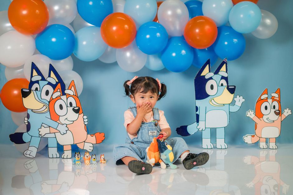 Adorable child sitting with cartoon characters at a colorful birthday party.