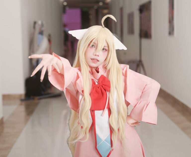 Charming cosplay featuring a fantasy character with long blonde hair and pink outfit inside a hallway.