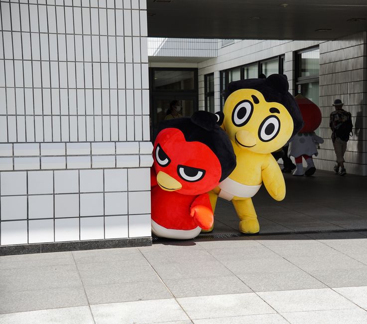 Vibrant mascot characters playfully peeking around a corner in a modern urban environment.